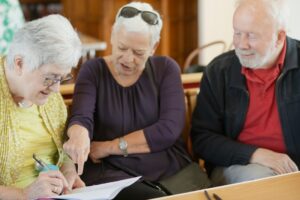 A senior couple sitting at a kitchen table reviewing Medicare documents with a pen and notepad.