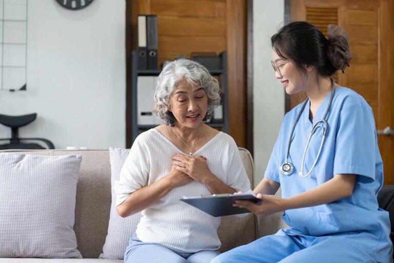 An older adult and a caregiver sitting together at a kitchen table, reviewing paperwork and smiling.