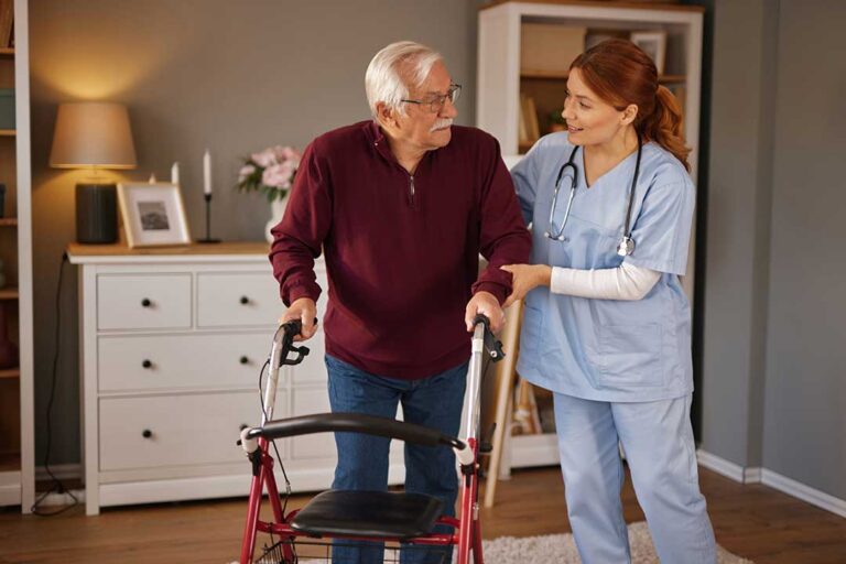 A senior adult using a walker, smiling, and moving independently through a brightly lit living room.